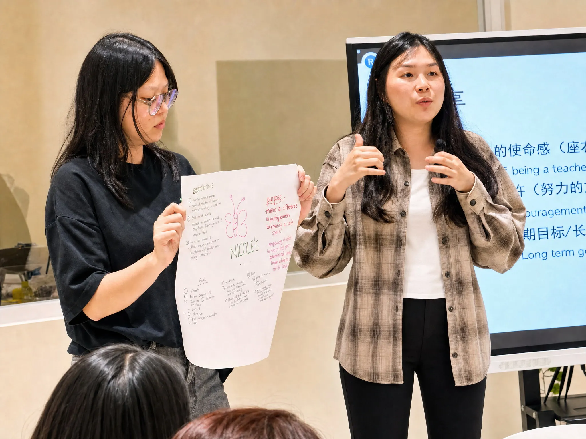 Two TITAN educators presenting at a staff training session, one holding up a hand-drawn sheet setting out her expectations, purpose and goals as a teacher
